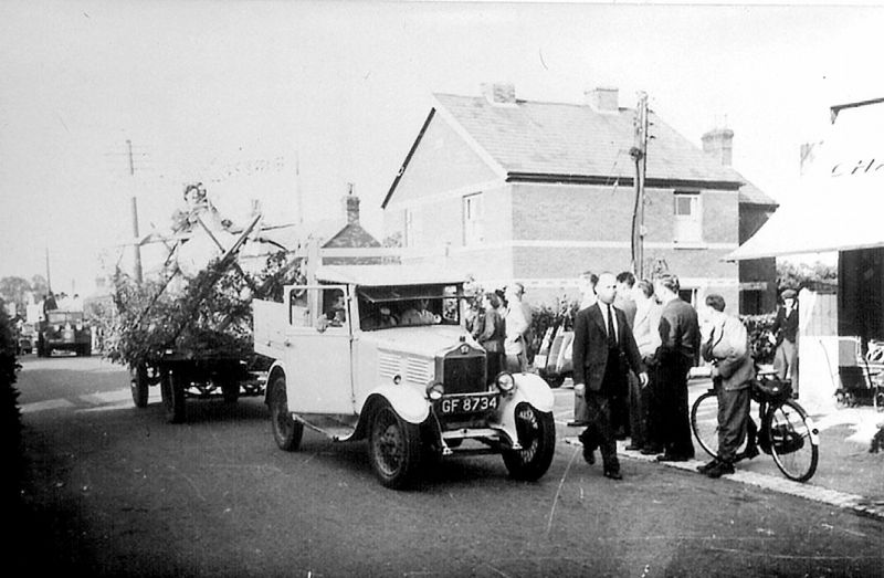  Carnival procession, outside Chatters Shop in High Street. Peter Farthing. Rutherford's pale blue truck GF8734. Banner on trailer is Councillor's Sprayer. 
Cat1 Mersea-->Events Cat2 Transport - buses and carriers