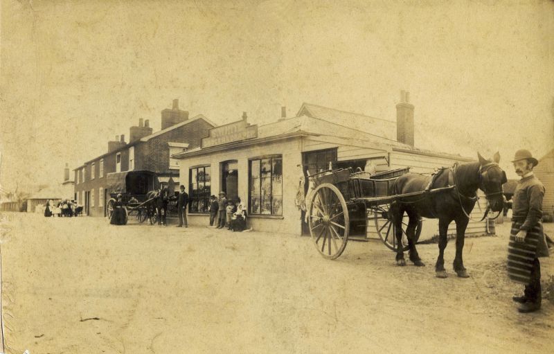  First shop on Mersea, owned by Sam White in Mill Road (opposite Free Church). The butcher on the right is Frank Rust. Frank was born c1865, dating this photo to around 1900.

Photograph lent by Tony Saye (Jack Saye's son).

Lions Talking Magazine 59 February 1983 has Dennis Chatters talking to Jack Saye about this shop. 
Cat1 Mersea-->Shops & Businesses Cat2 Transport - buses and carriers