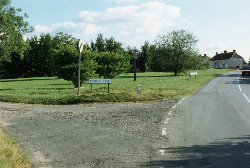  Pudding Green, with Pudding Lane on left, Birch village sign on green, and view up hill to to Winstree Cottages. 
Cat1 Birch-->Road Scenes