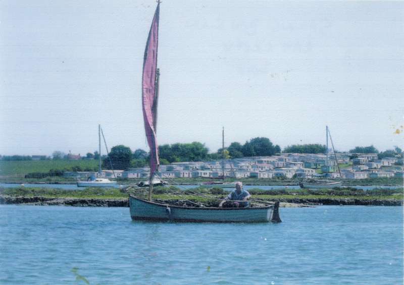  Des Carter sailing the 'small' BEN GUNN in Ray Creek. 

Simmons' Caravan Park in background 
Cat1 People-->Other Cat2 Yachts and yachting-->Sail-->Small yachts / dinghies Cat3 Mersea-->Creeks, fleets, channels, saltings